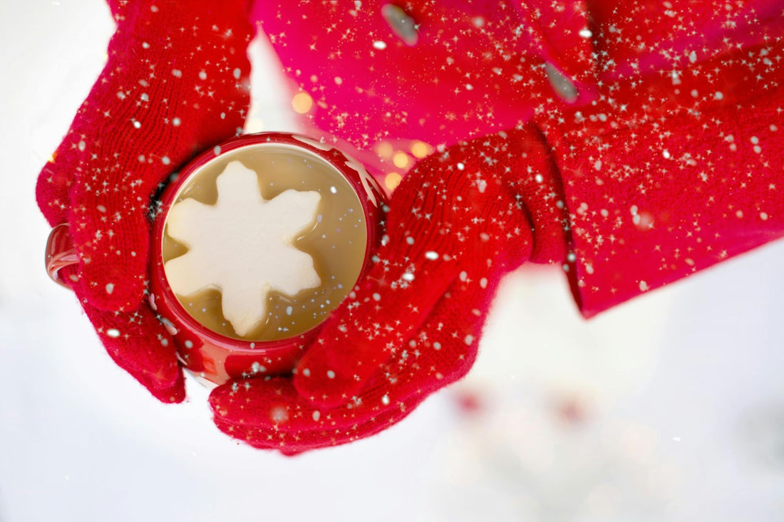 Gloved hands holding a warm cup of hot chocolate while snow is falling