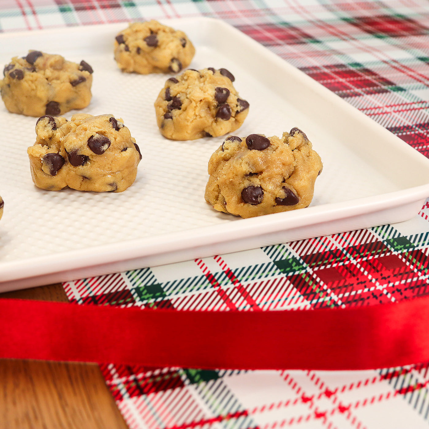 Chocolate chip cookie dough on a white plate with a holiday tablecloth in the background