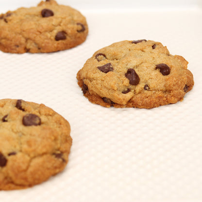 Three chocolate chip cookies on a white surface