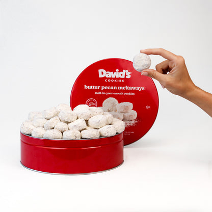 Red tin of David's Cookies butter pecan meltaways with a hand holding a cookie.